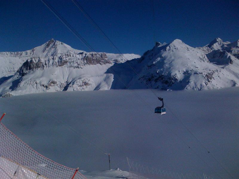 Un télésiège suspendu au-dessus d'une montagne enneigée, avec un ciel bleu en arrière-plan.