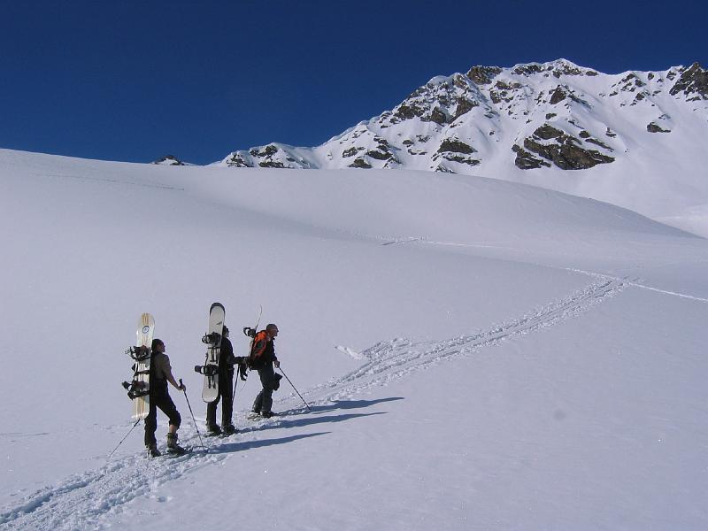 Trois personnes marchent sur une pente enneigée, entourées de neige fraîche et d'un paysage hivernal.
