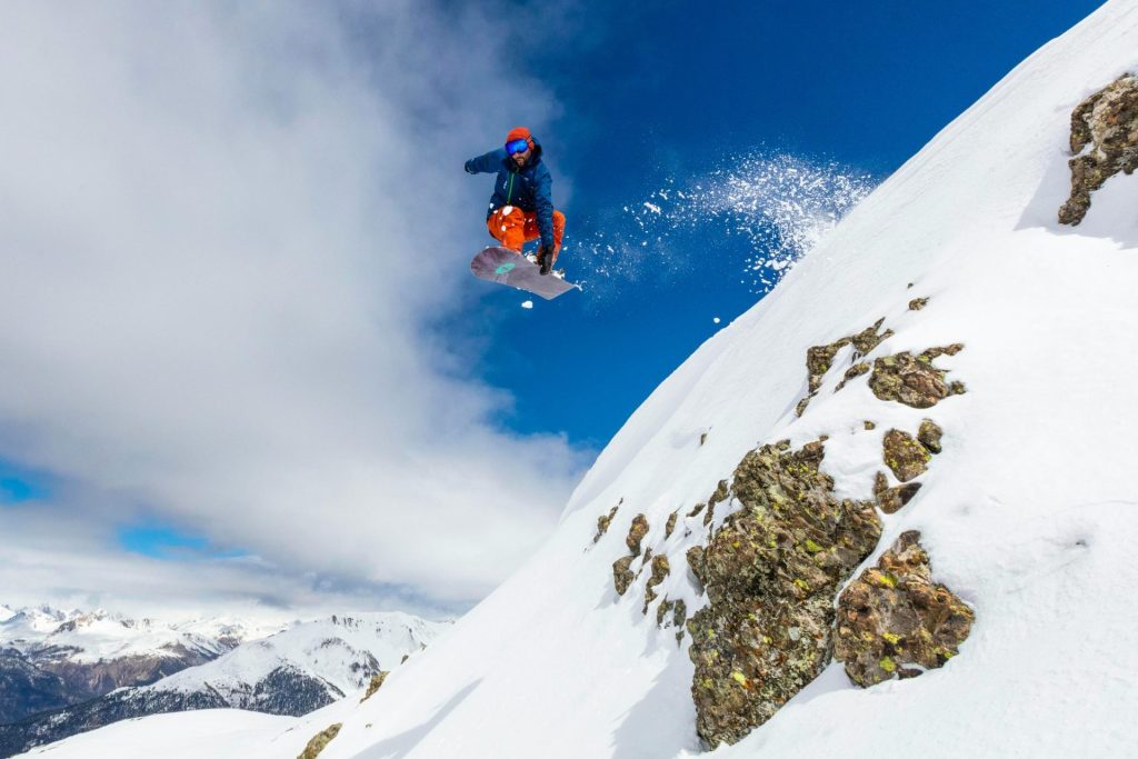 homme en veste rouge et pantalon bleu assis sur une montagne enneigée en plein jour